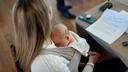 A woman sits while an infant rests on her chest. A woman sits while an infant rests on her chest.