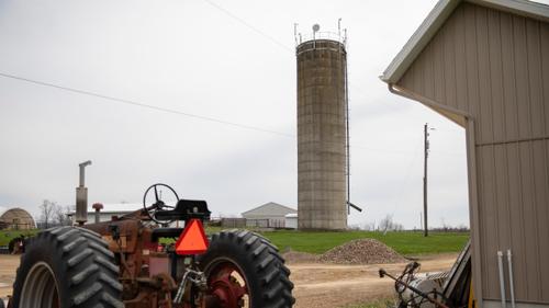 A tractor in the foreground and a radios and a microwave dish providing internet service installed atop a farm silo in the background. A tractor in the foreground and a radios and a microwave dish providing internet service installed atop a farm silo in the background.