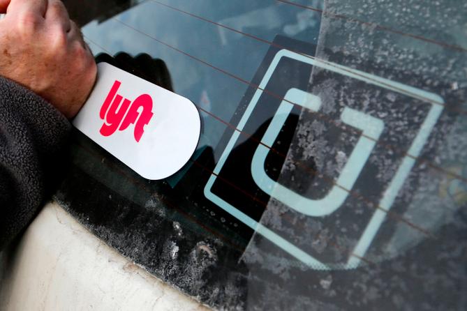 In this 2018, file photo, a Lyft logo is installed on a car next to an Uber sticker in Pittsburgh. In this 2018, file photo, a Lyft logo is installed on a car next to an Uber sticker in Pittsburgh.