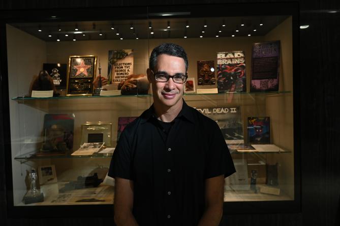 Adam Lowenstein stands in front of a display case of horror artifacts. Adam Lowenstein stands in front of a display case of horror artifacts.