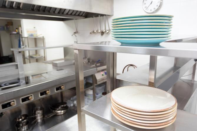 A stock image of plates stacked on a stainless steel shelf in a kitchen