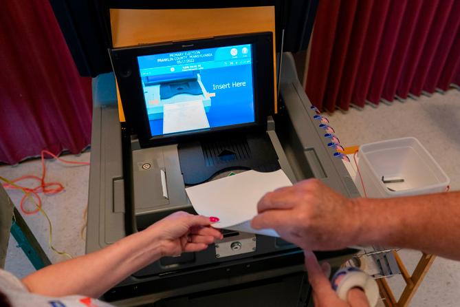 A polling judge, right, helps guide a voter's ballot into a voting machine during the Pennsylvania primary election, at Mont Alto United Methodist Church in Alto, Pa., on May 17, 2022. A polling judge, right, helps guide a voter's ballot into a voting machine during the Pennsylvania primary election, at Mont Alto United Methodist Church in Alto, Pa., on May 17, 2022.